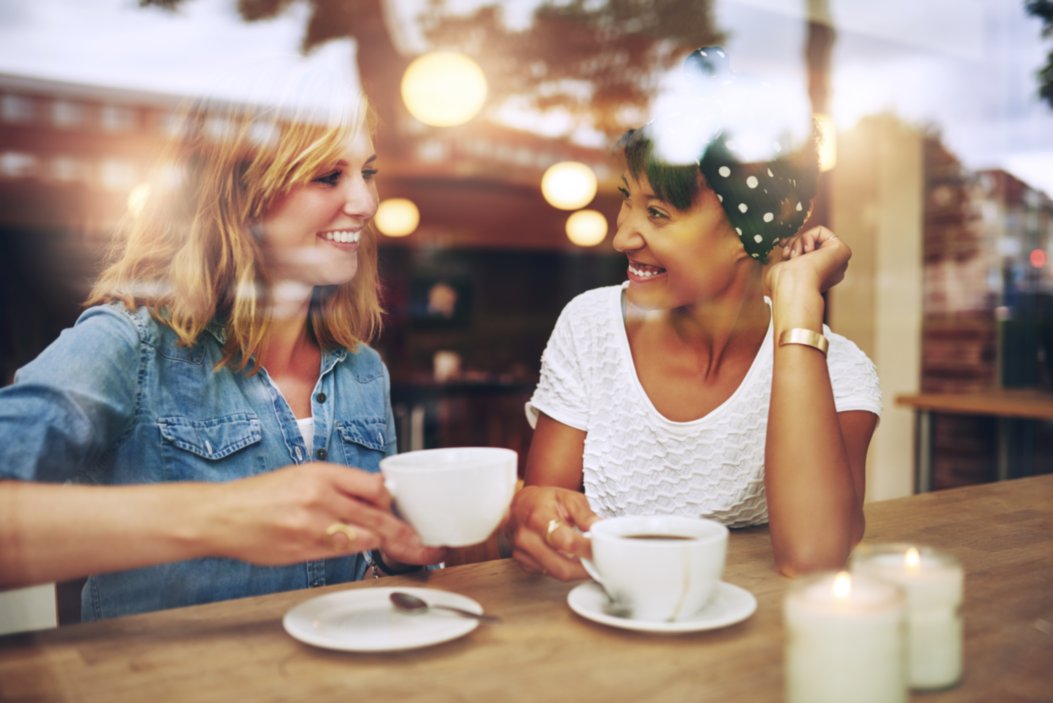 Blonde and brunette woman smiling and drinking coffee